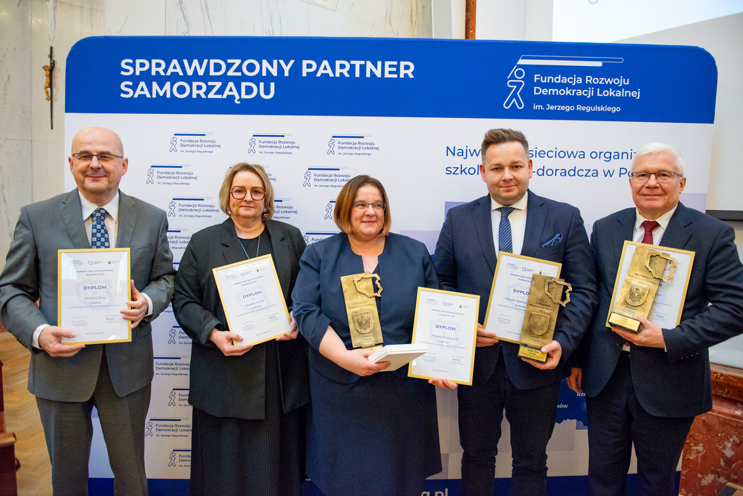 Fot. mat. pras. Ośrodka Kształcenia Samorządu Terytorialnego im. Waleriana Pańki Prezydent Gliwic Adam Neumann pozujący na ściance z innymi nagrodzonymi prezydentami