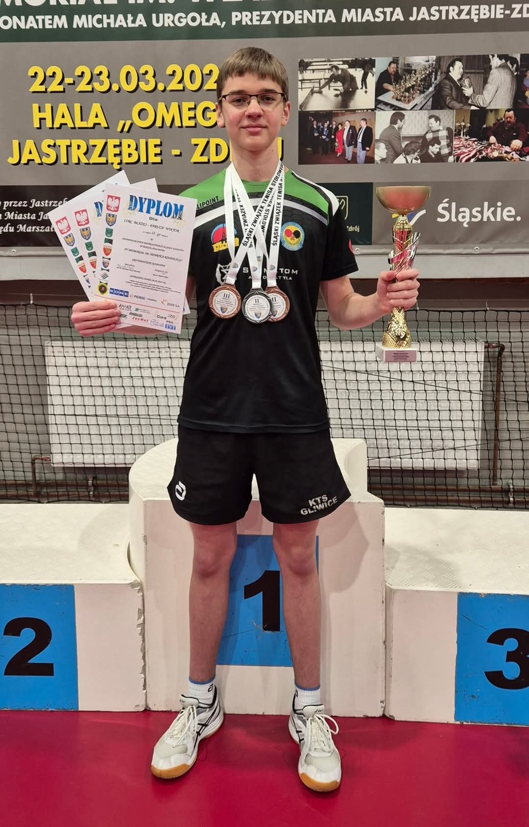Wiktor Paruch pozujący na tle podium z medalami i dyplomami