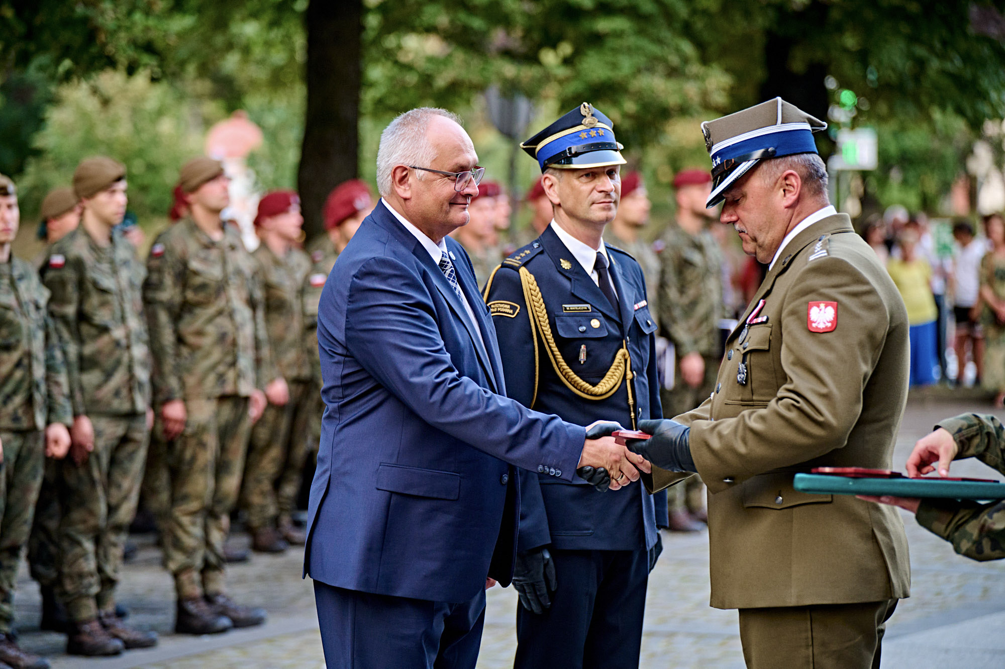trzech ludzi składa sobie uścisk dłoni, wokół inni ludzie