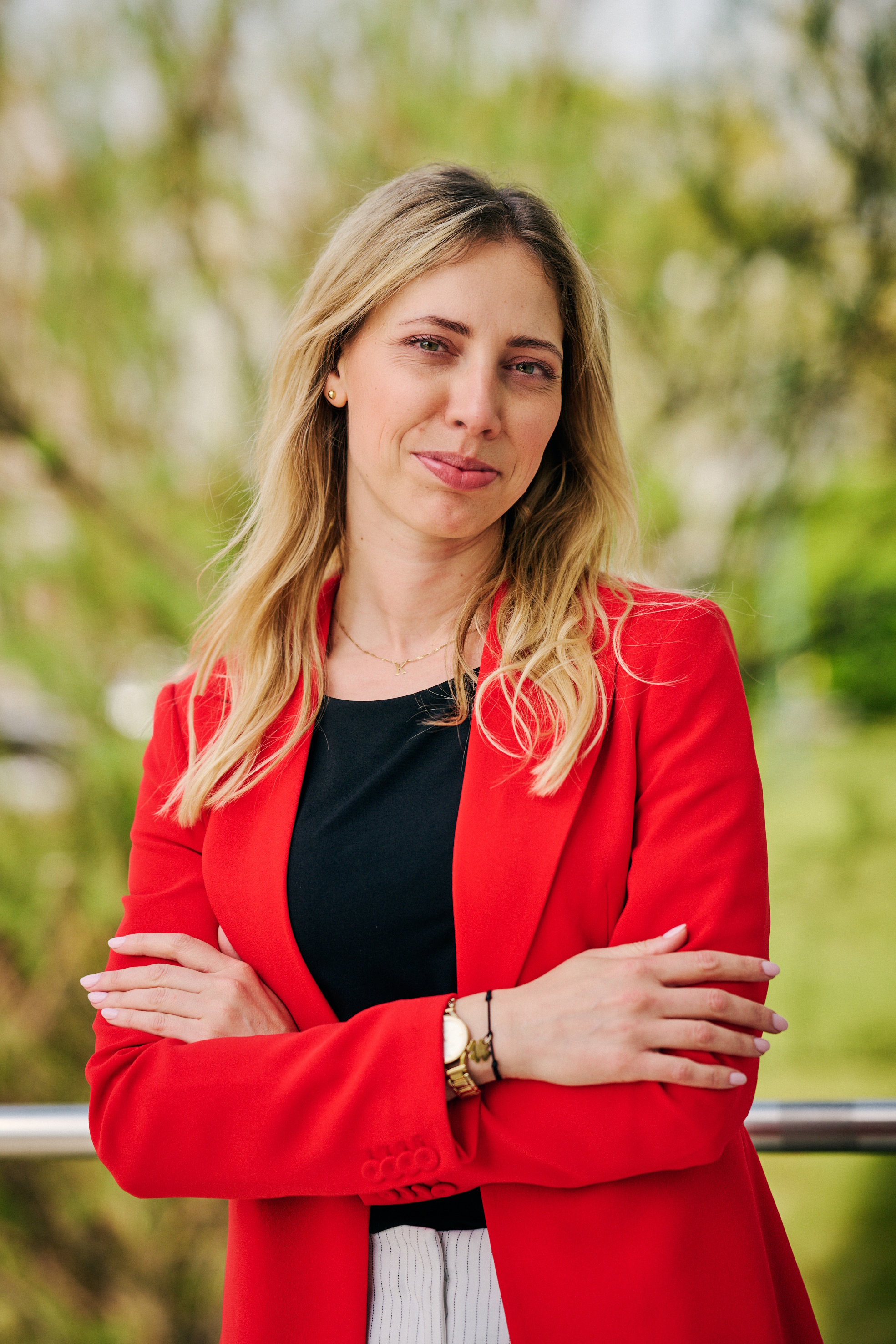 Kinga Kamińska w czerwonej marynarce. Uśmiecha się do aparatu