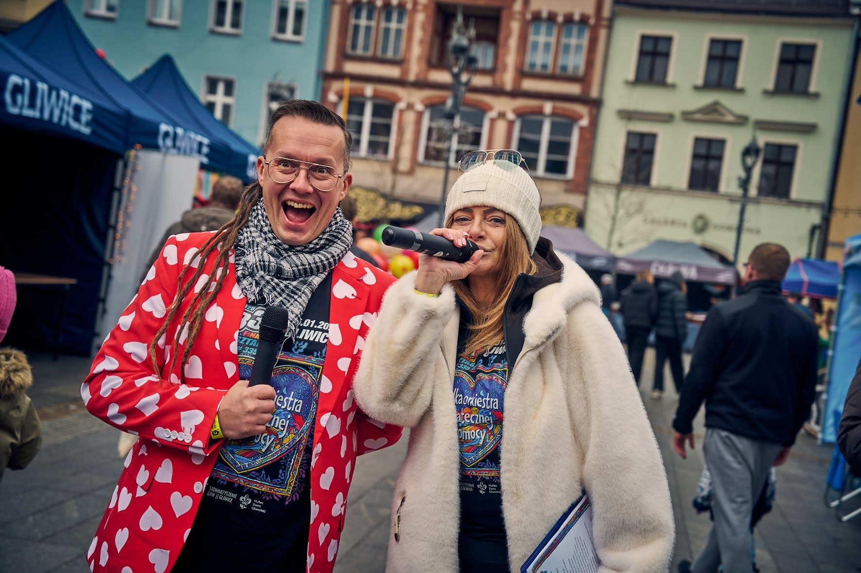 Fot. M. Buksa/UM w Gliwicach Uśmiechnięty mężczyzna w czerwonej marynarce z białymi serduszkami, obok niego kobieta z mikrofonem