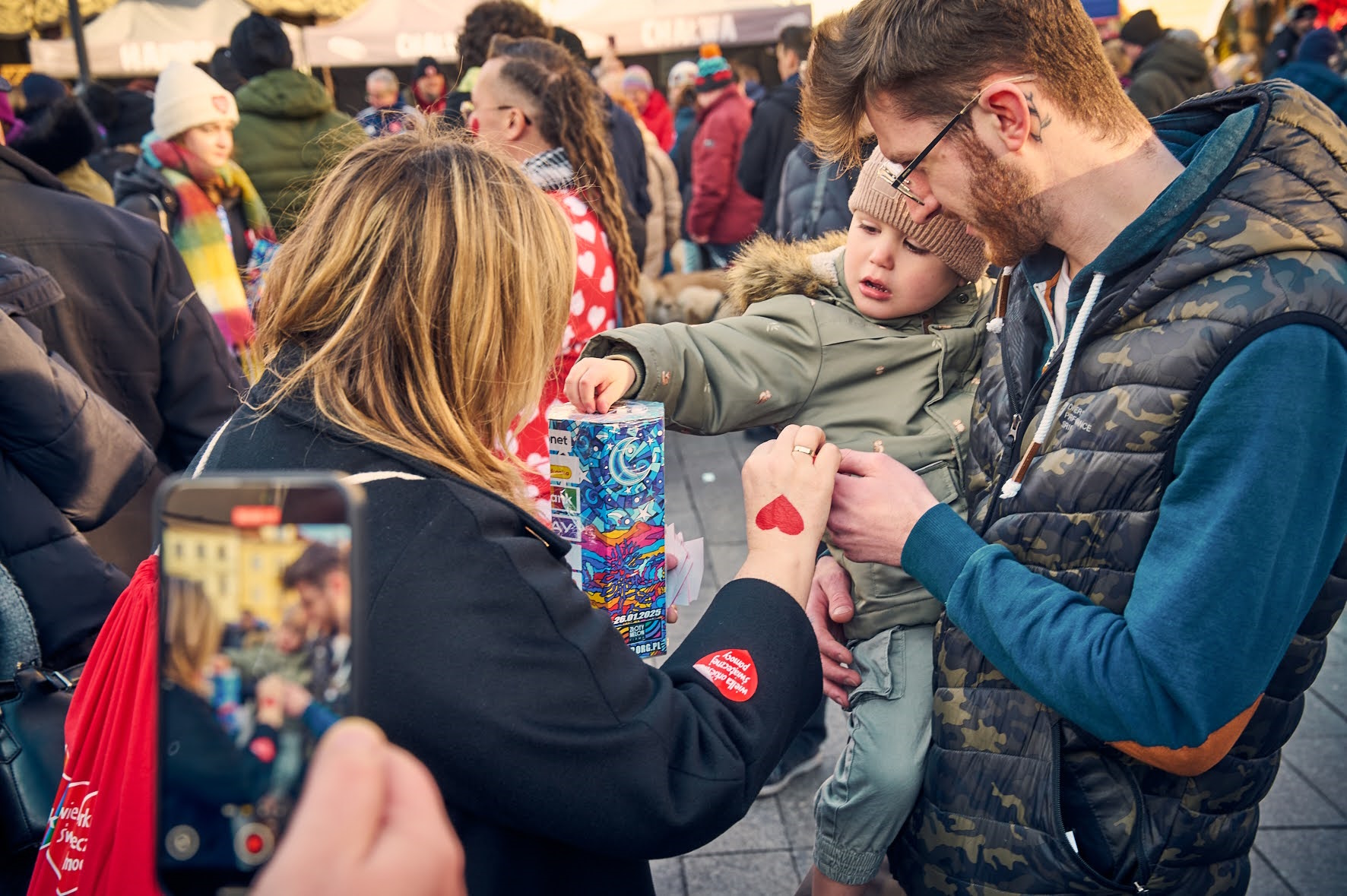Fot. M. Buksa/UM w Gliwicach Mężczyzna z chłopcem na rękach, chłopiec wrzuca pieniądze do puszki, którą trzyma prezydent Kuczyńska-Budka