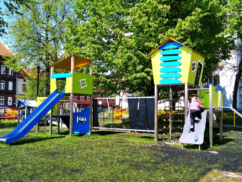 zielone domki na placu zabaw, wśród zieleni. Na placu dziewczynka