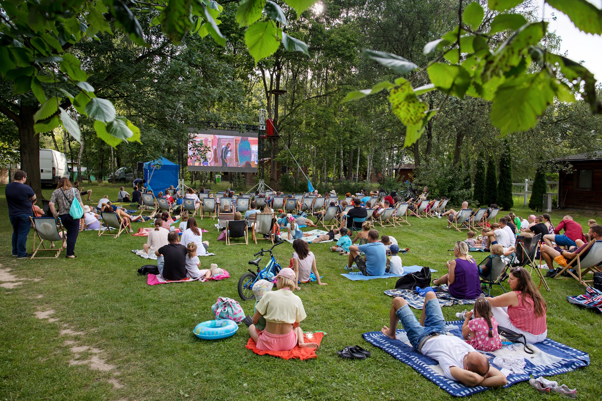 ludzie na kocach w plenerze, oglądają film na ekranie